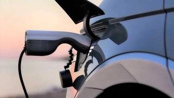 Electric vehicle plugged in using bidirectional charger at sunset