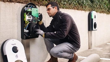 Technician inspecting internal components of an EV charger outdoors.