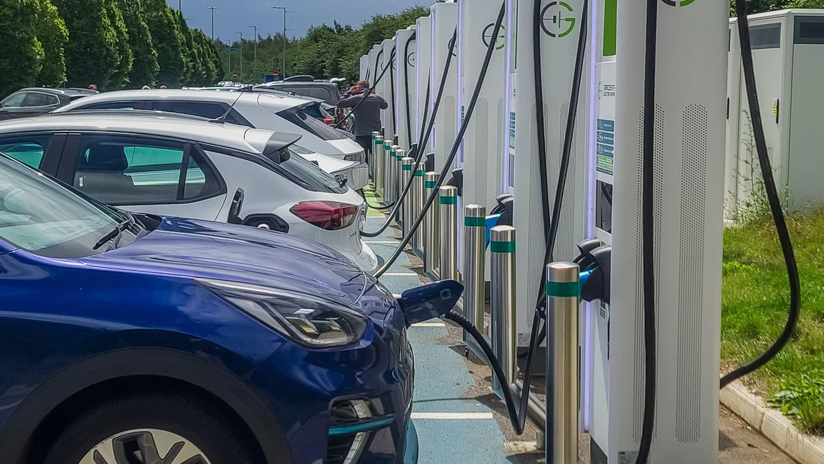 Multiple EVs are plugged into high-power public charging units in a busy car park